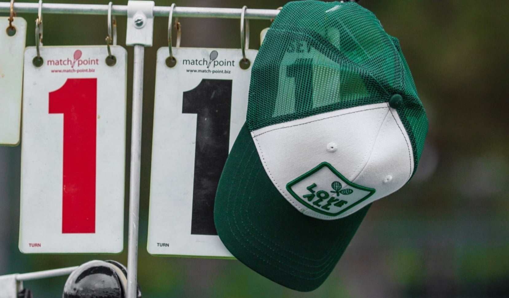 A white trucker hat with a dark green mesh back hanging on a hook, displaying a logo on the front.