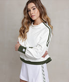 A female model wearing a white crewneck pullover with green trim on the waistband, cuffs, and shoulders. The pullover has a mock neck and zipper details on the sides.
