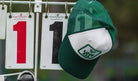 A white trucker hat with a dark green mesh back hanging on a hook, displaying a logo on the front.