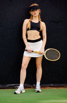 woman wearing a white tennis skirt with a black band and holding a tennis racquet.
