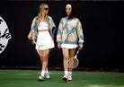 two women holding tennis racquets and wearing tie dye sweatshirts and white tennis skirts