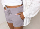 A person wearing lilac-colored sporty shorts with a drawstring waist, paired with a white top. The image shows the person from the waist down, focusing on the shorts.
