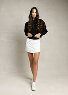 model wearing white tennis skirt with black band and a black sweatshirt